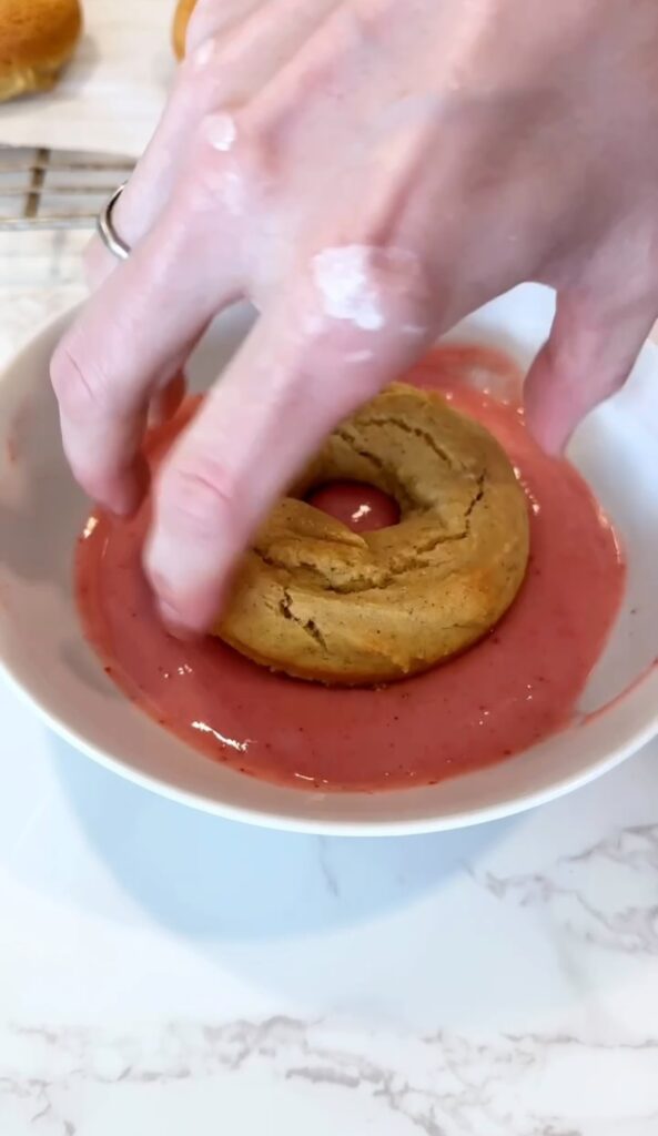 dipping baked gluten free donuts into strawberry glaze